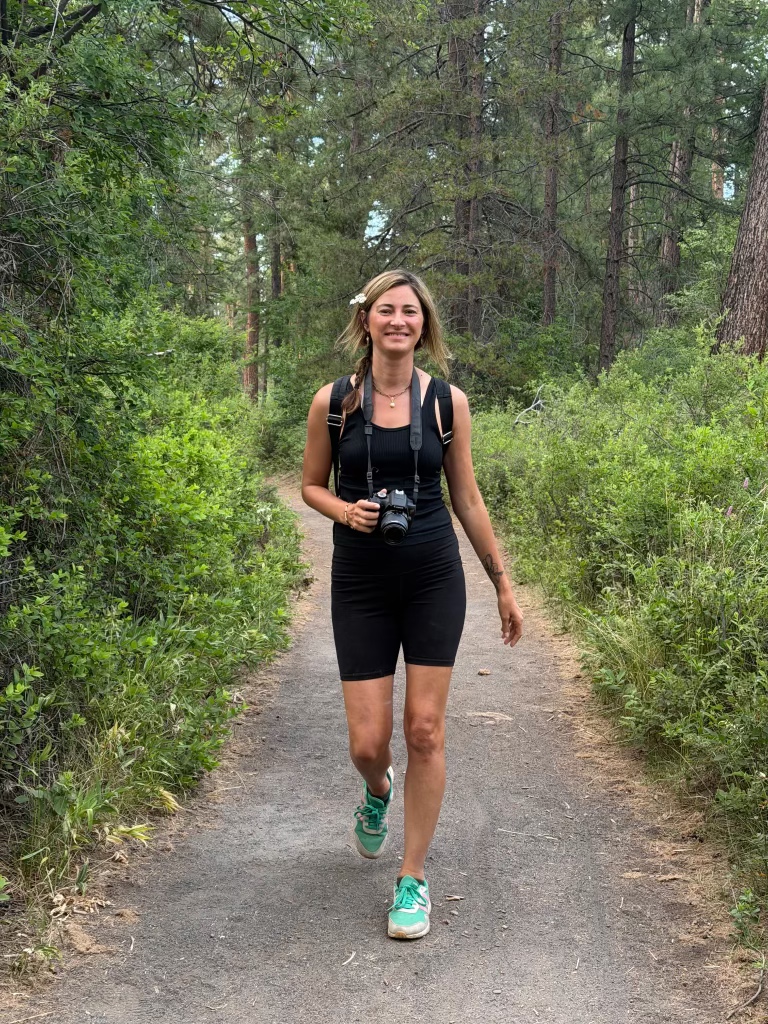 Moriah Brown walking on a forest path holding a camera